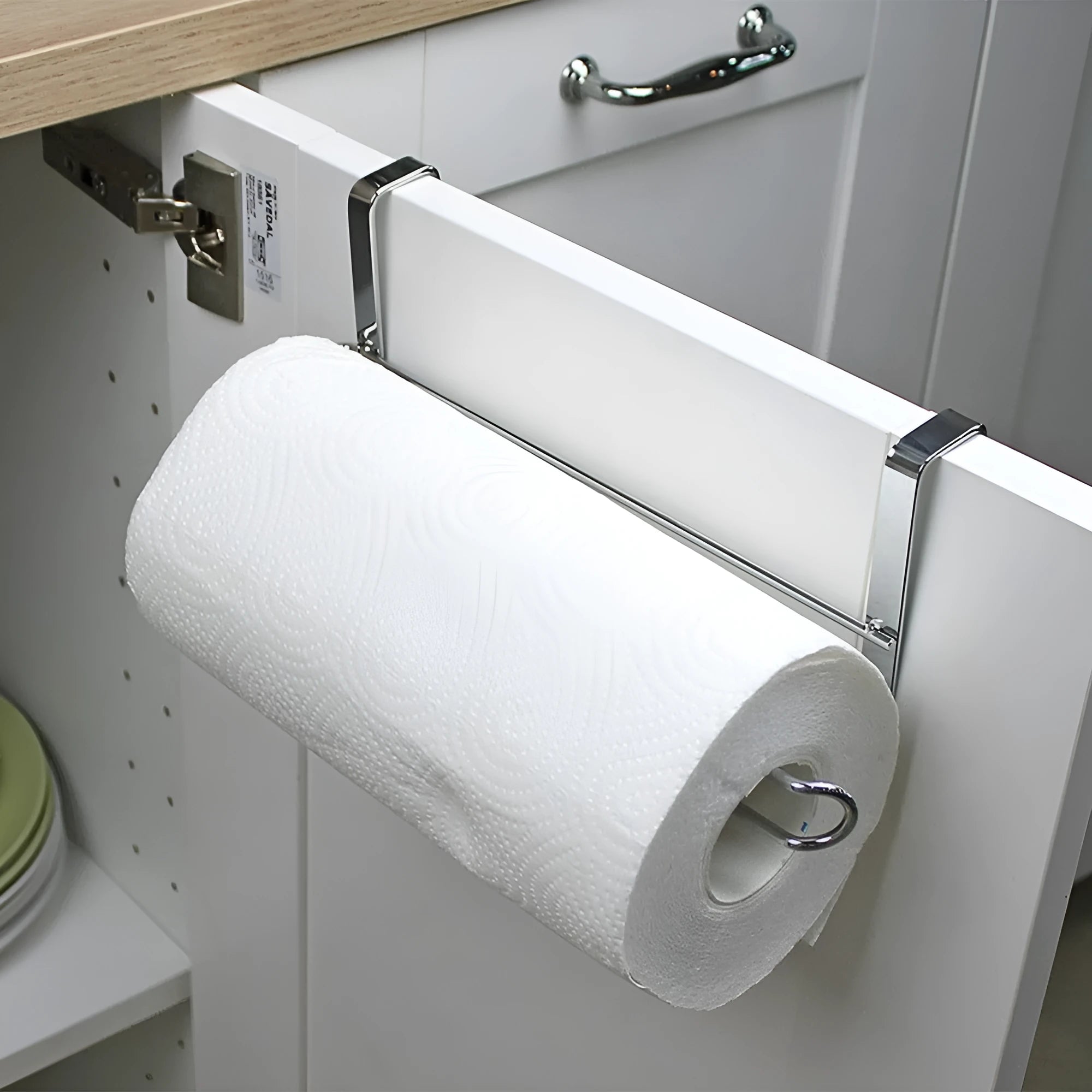 Silver stainless steel rack hanging on the back of a kitchen cabinet door holding a paper towel roll.