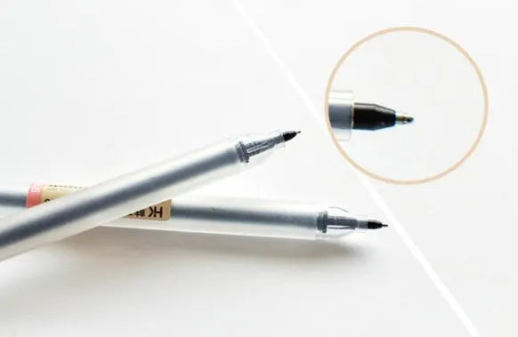 Pack of twelve black Muji gel pens with 0.5mm nibs, caps removed, on a notepad.