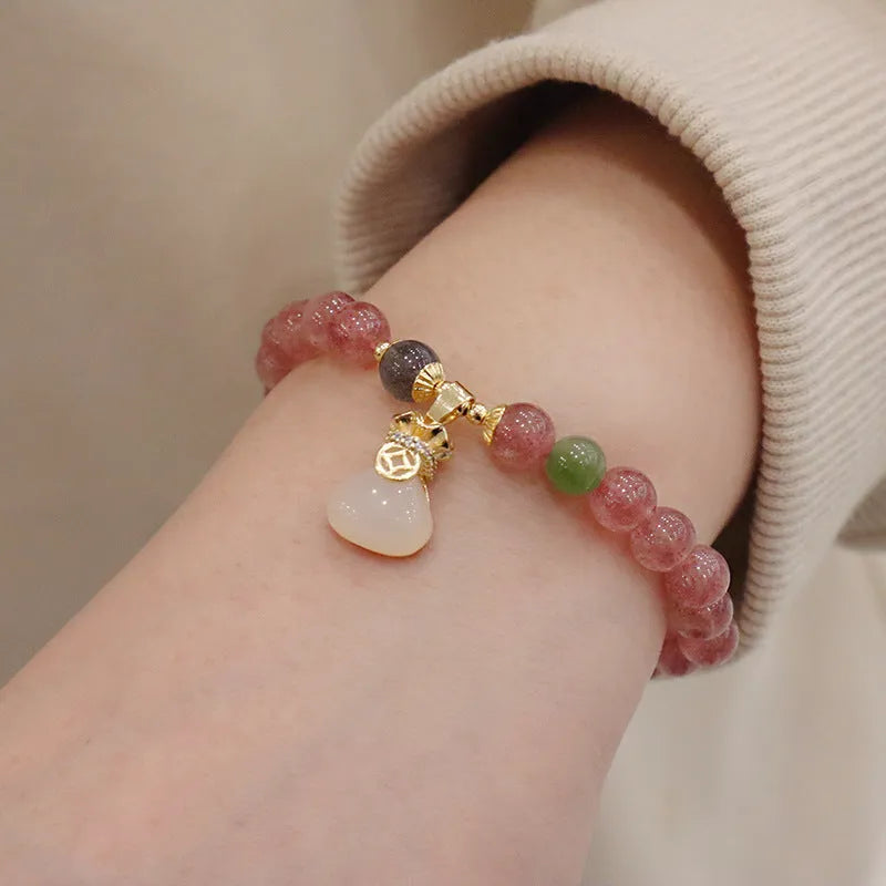 Women's strawberry quartz bracelet with geometric stones, purse charm and lucky bagg charm on wrist