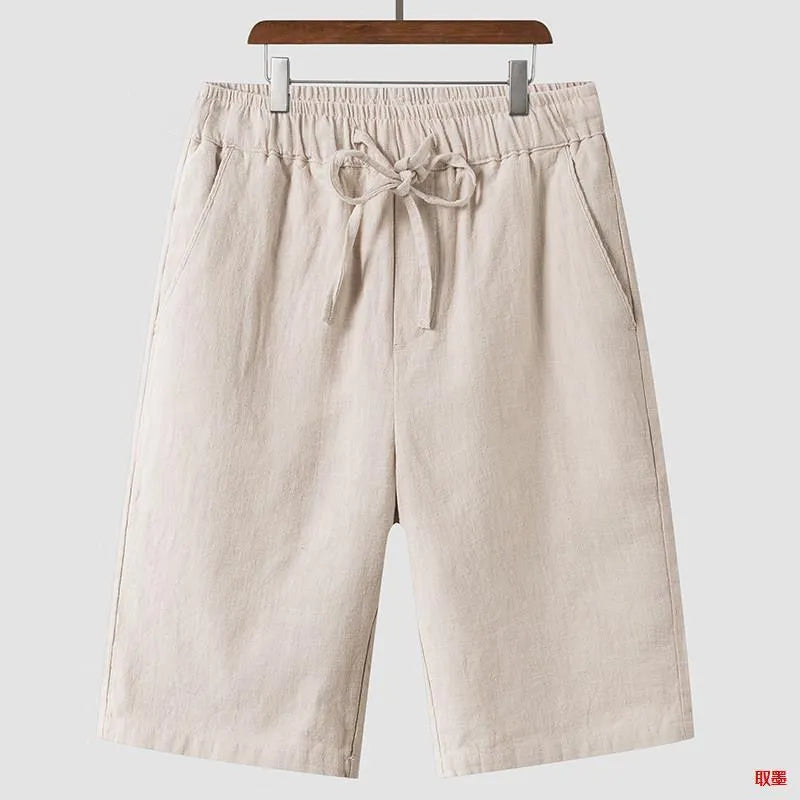 Pair of beige men's casual linen shorts with a loose fit and cropped length on a plain background.