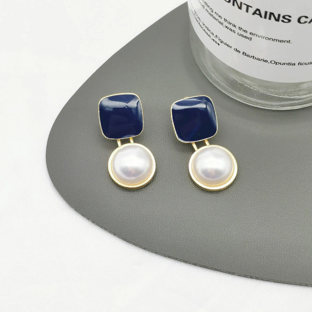 Red and blue geometric alloy stud earrings with pearl centre on neutral background