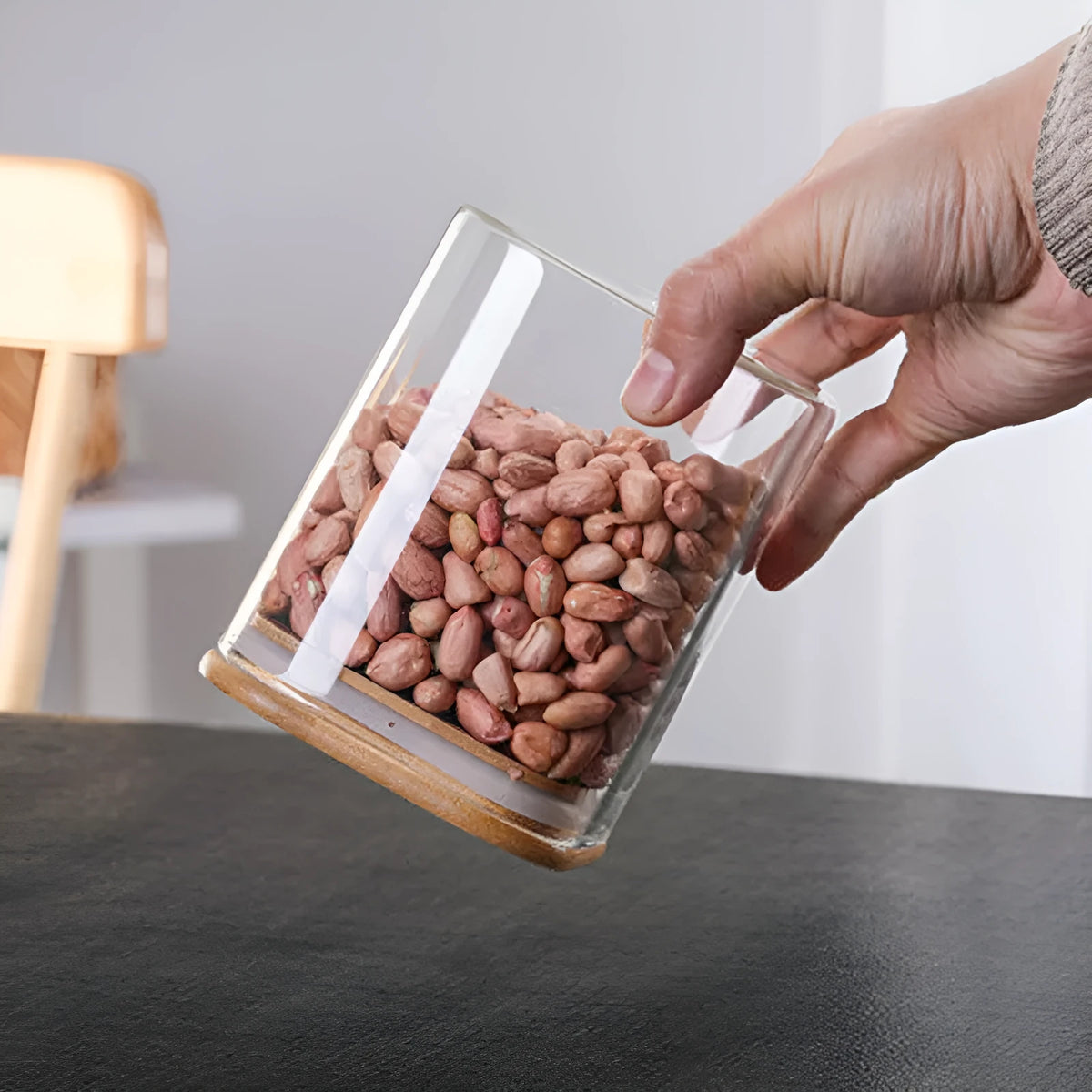 Square glass storage jar for coffee beans with wooden spoon on kitchen counter, clear body shows contents