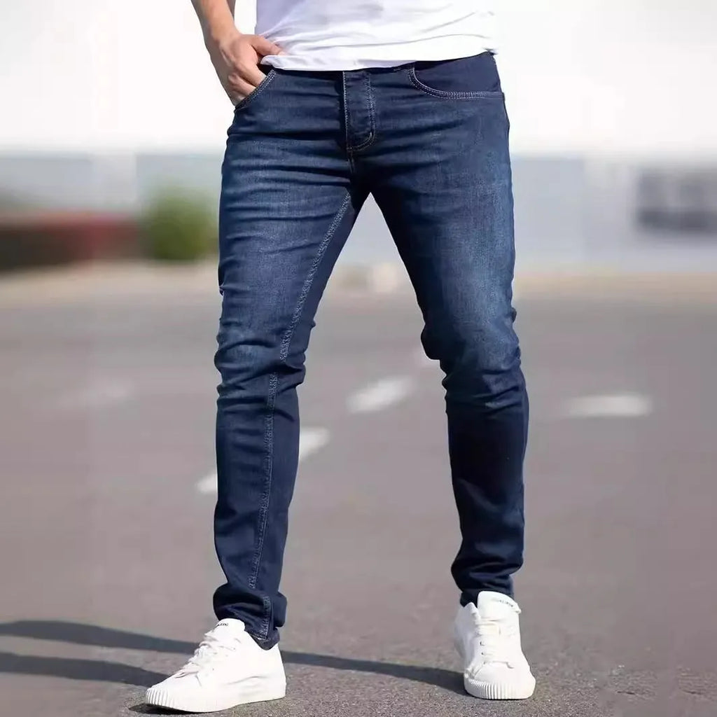 Men's dark blue slim-fit skinny jeans on a hanger, showing mid-waist and zipper fly detail.