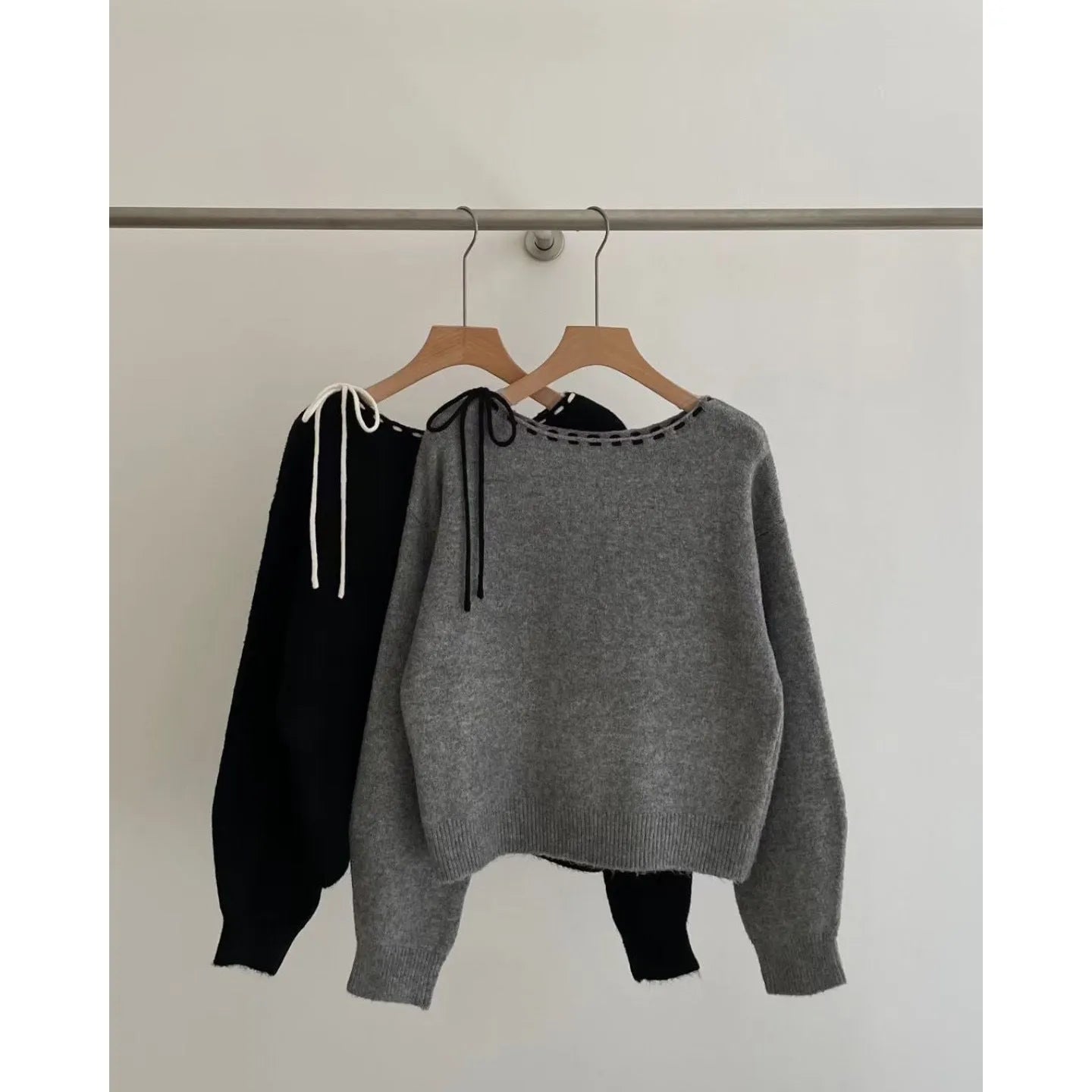 A grey women's loose-fitting knitwear pullover on a hanger, showing its casual style.