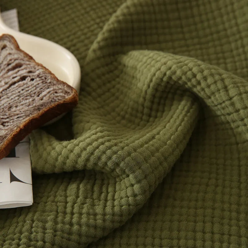 Cotton four-layer gauze blanket with tassel trim in avocado green colour, laid flat.