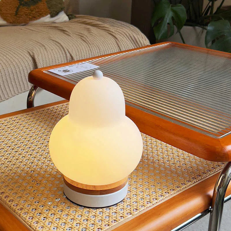 White pear-shaped rechargeable touch LED table lamp with PE shade on a wooden bedside table