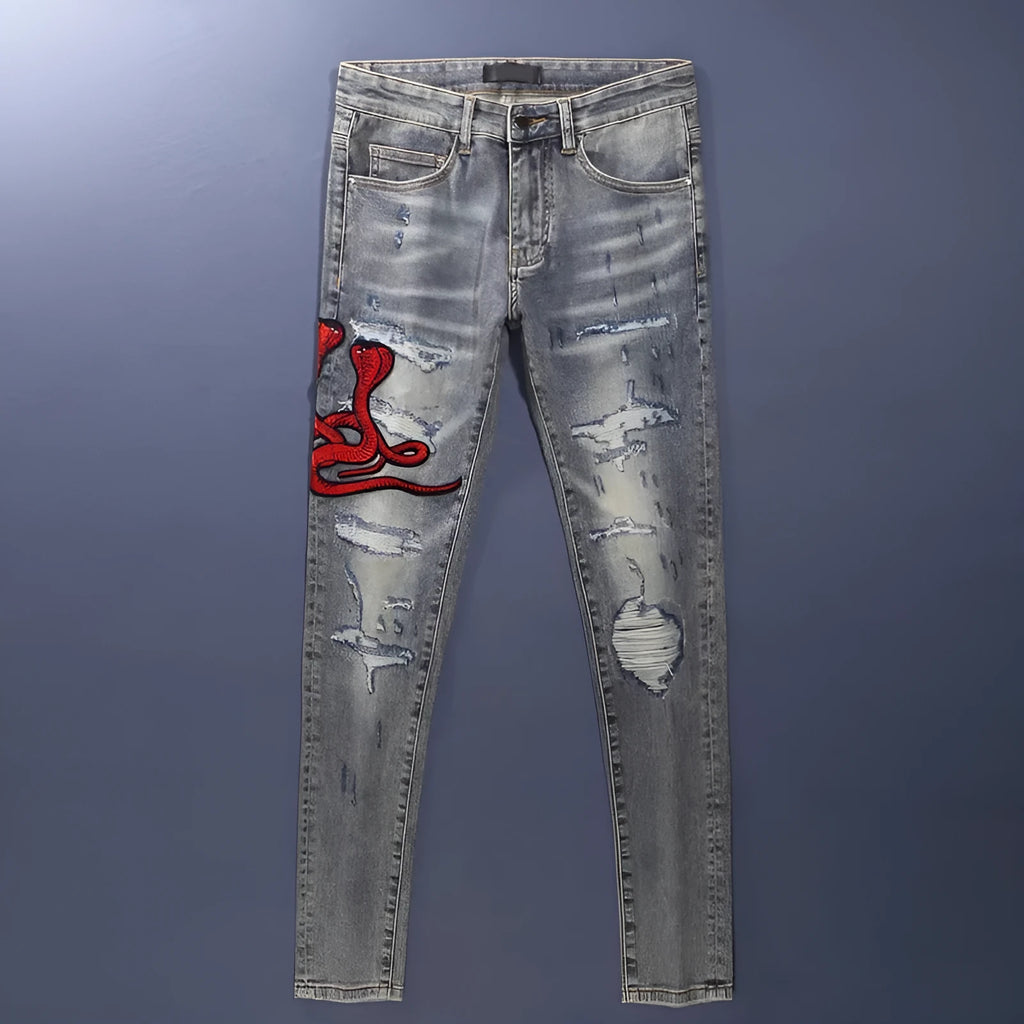 Man wearing slim-fit light blue jeans with distressed knee patches and embroidered back pocket detail.