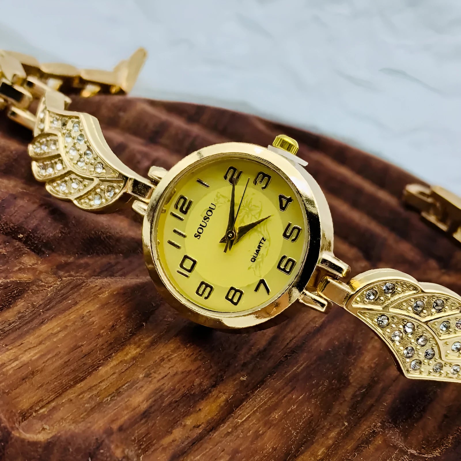 A stainless steel women's watch with a round dial on a metal strap, showing a gold-coloured face.