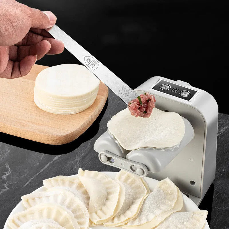 White automatic electric dumpling maker machine with USB charging cable, brush, and spoon on a kitchen counter.