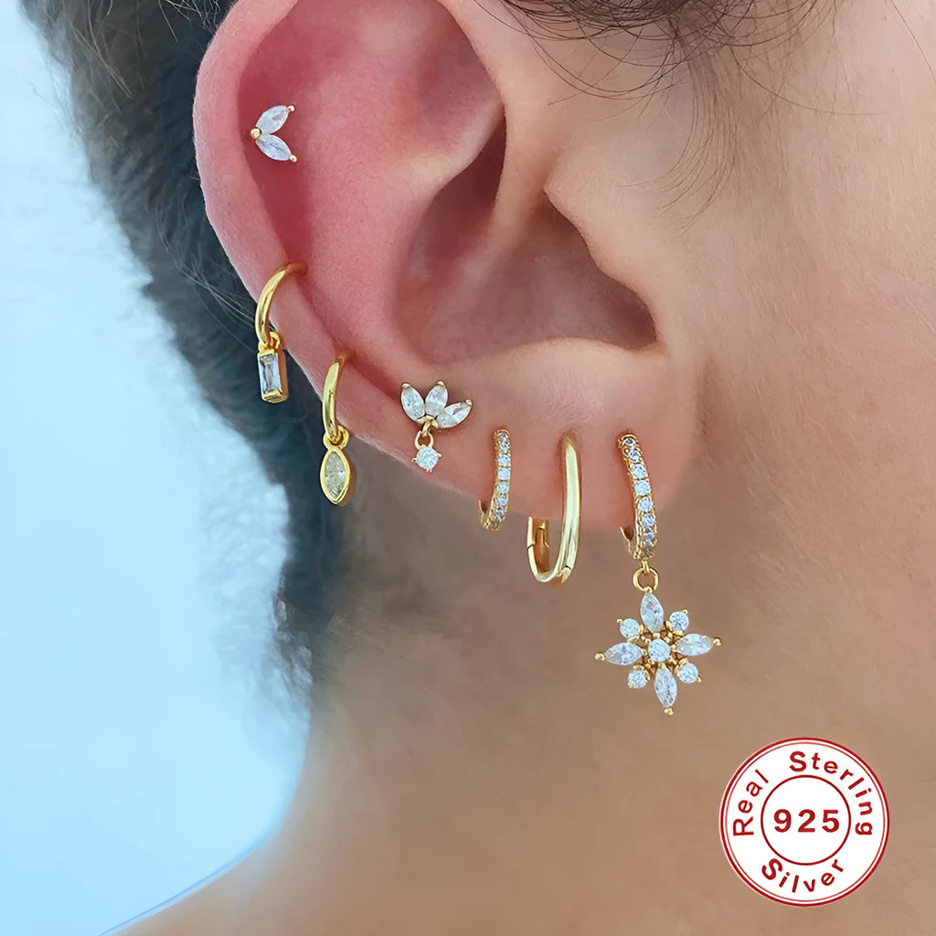 A pair of sterling silver snowflake pendant earrings with a gemstone, shown in yellow gold and white gold colour finishes.