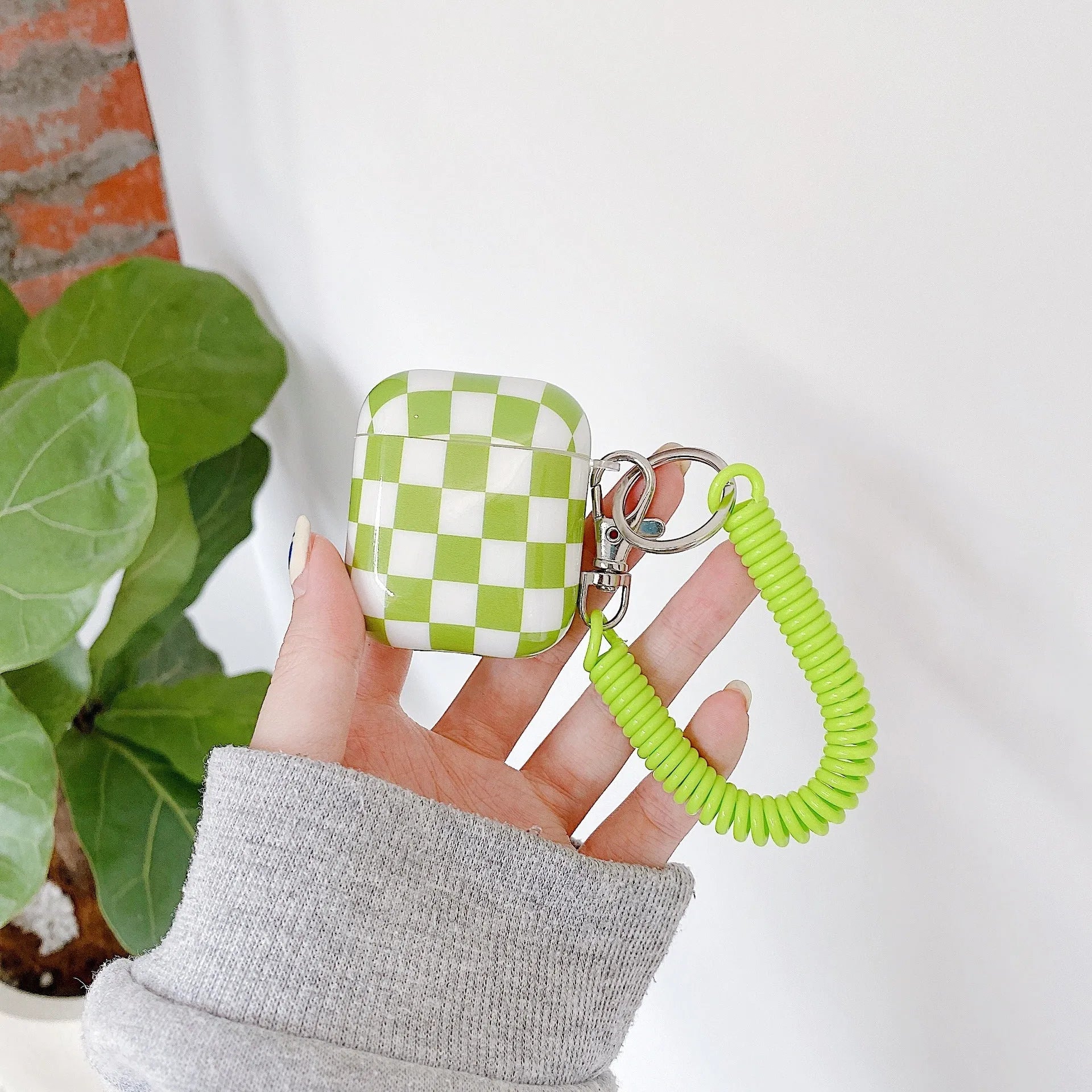 Black and green checkerboard pattern TPU protective case sleeves for Apple AirPods, one with a smiley face lanyard attached.