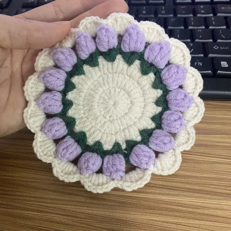 Handmade woven floral coaster in cotton and linen yarn on a wooden table