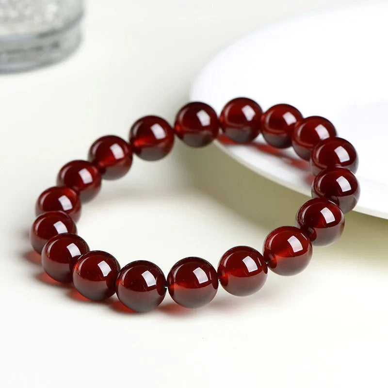 Close-up of a natural orange red garnet bead bracelet with a metal Ruyi charm on a wrist.
