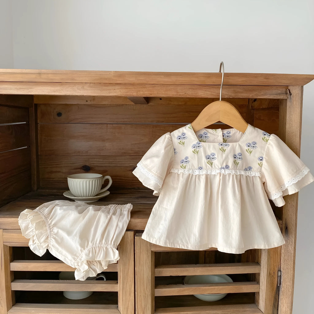 Apricot cotton two-piece suit with floral pattern, square collar top, and wooden horn buttons, next to matching bloomer pants.