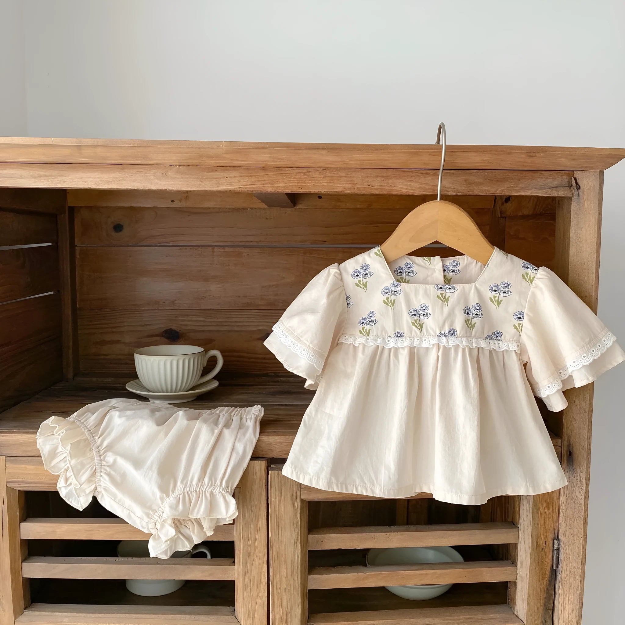 Apricot cotton two-piece suit with floral pattern, square collar top, and wooden horn buttons, next to matching bloomer pants.