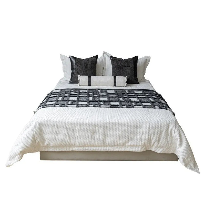 Modern grey and white plaid bed runner blanket set with round leather pillow on a bed.