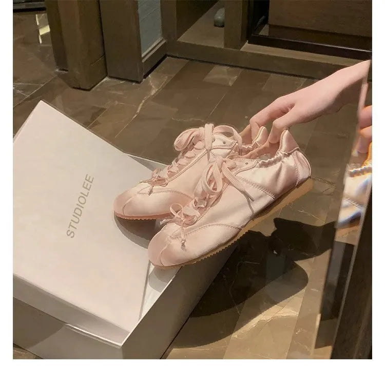 Women's satin ballet flats in champagne pink with round toe and front lace-up closure.