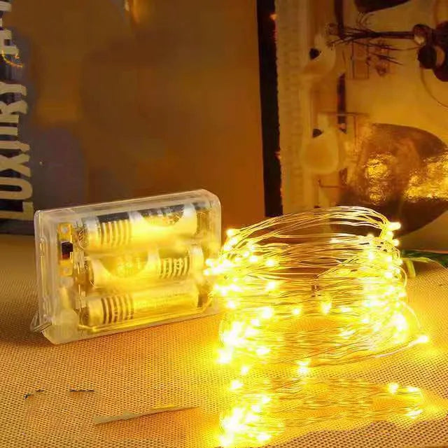 Flexible copper wire string light with 120 LEDs wrapped around a branch, showing battery box and USB connection.