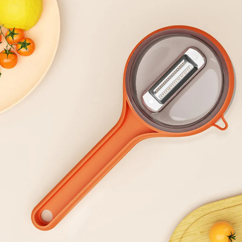Light green kitchen peeler with a small orange storage bucket attached underneath the blade.