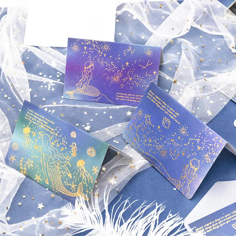 Set of three bronzing mermaid-style folded greeting card envelopes in celestial colourways, 13x8.5cm, on a light background