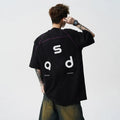 Man wearing a loose-fitting black cotton T-shirt with a white letter print on the chest.