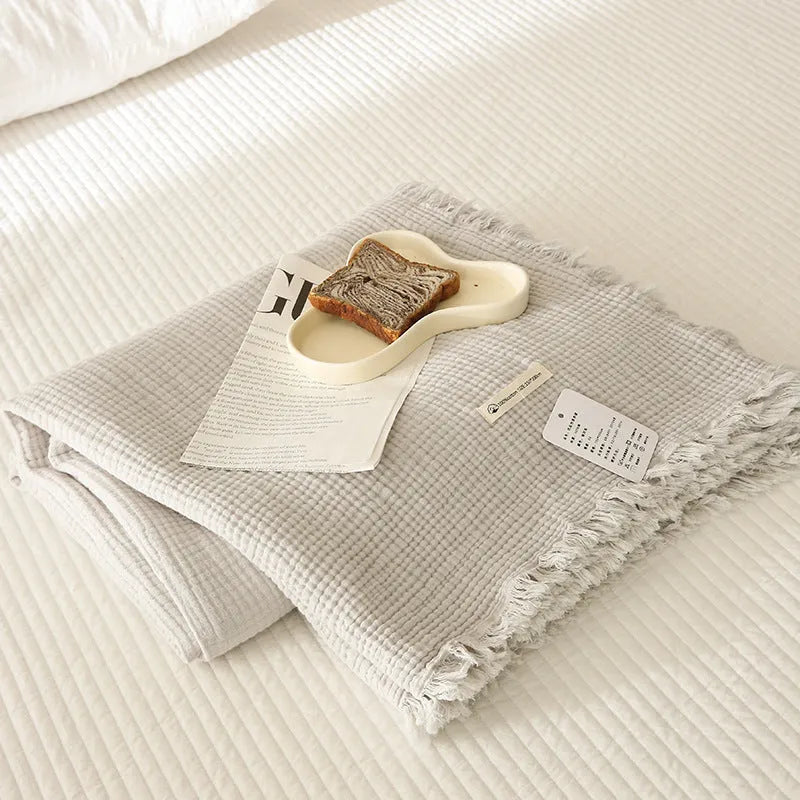 Cotton four-layer gauze blanket with tassel trim in avocado green colour, laid flat.