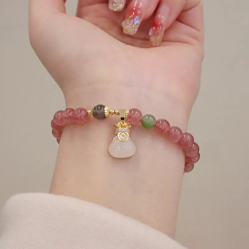 Women's strawberry quartz bracelet with geometric stones, purse charm and lucky bagg charm on wrist