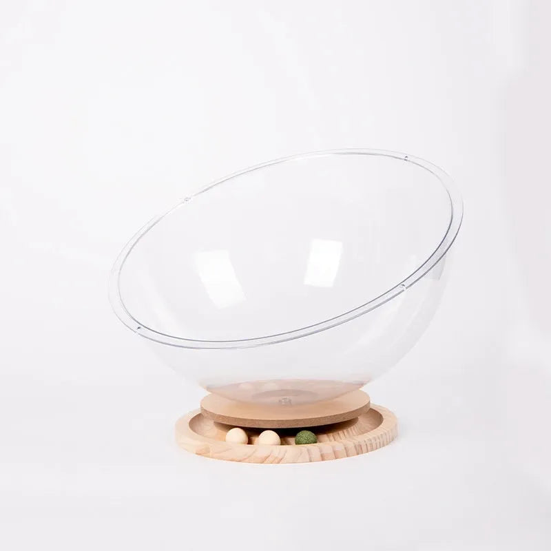 Transparent acrylic space capsule cat bed with a turntable base on a wooden floor.