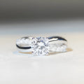 Silver ring with 1 karat moissanite in four-claw setting on a geometric twisted arm band.