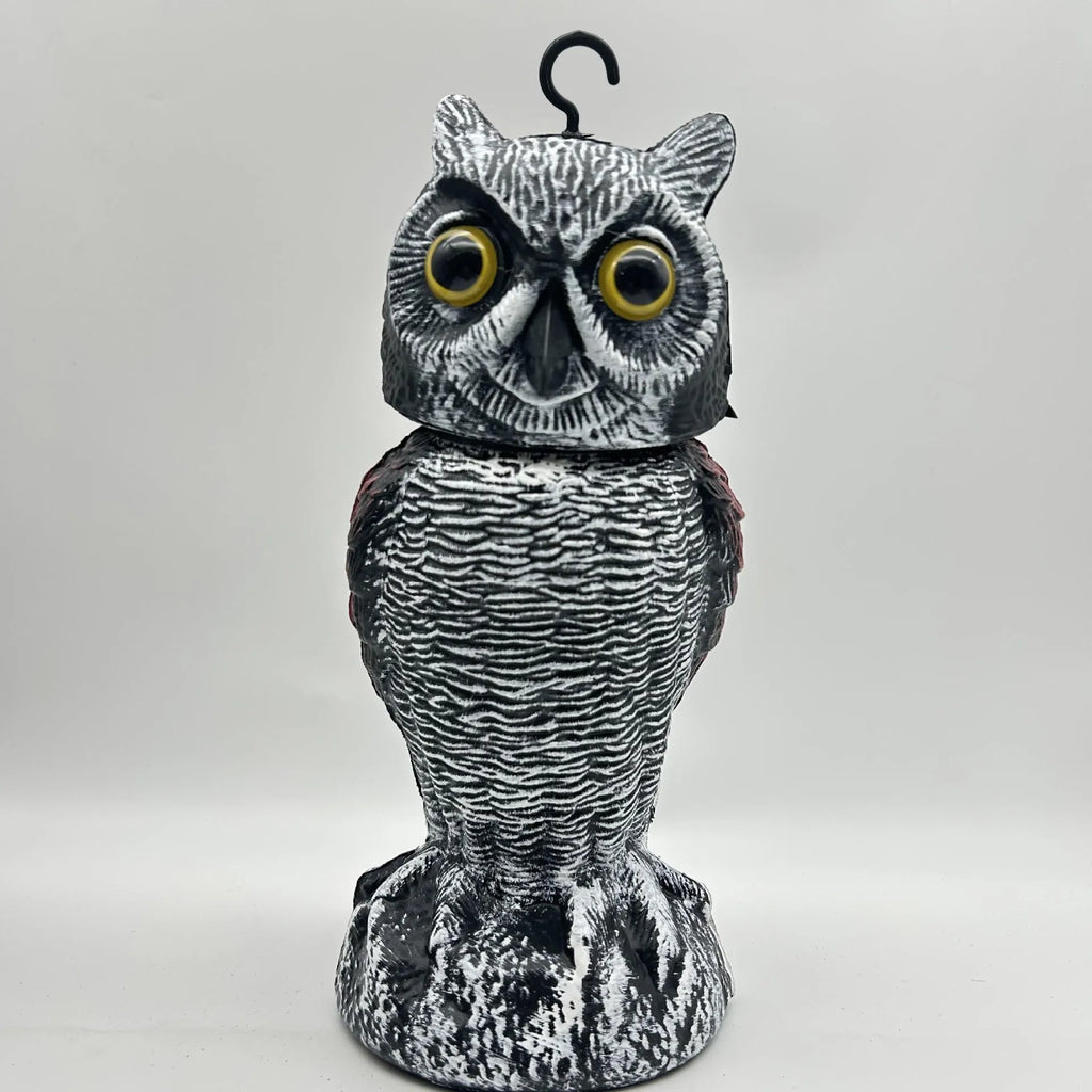 Plastic artificial owl bird scarer with a shaking head, shown in a garden setting.