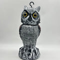 Plastic artificial owl bird scarer with a shaking head, shown in a garden setting.