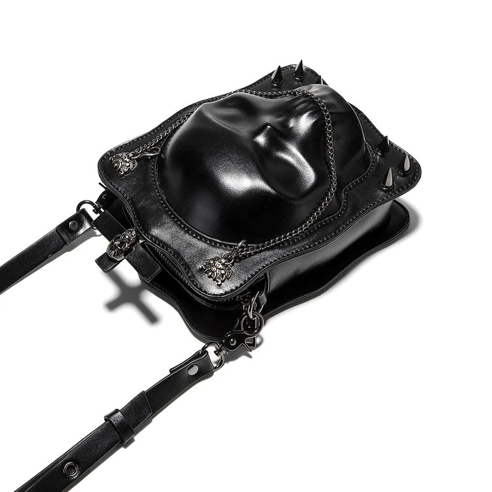 Black square crossbody bag with embossed skull design and metal chain strap against dark background