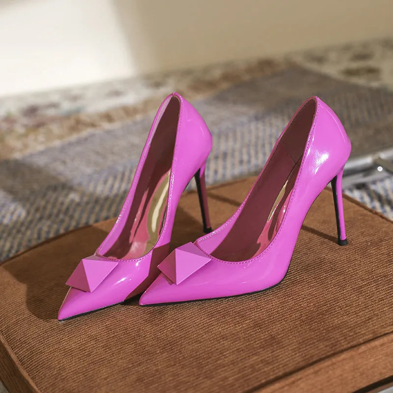 Pink patent leather women's stiletto heels with pointed toe, buckle strap, and rivet detail on a shallow cut.