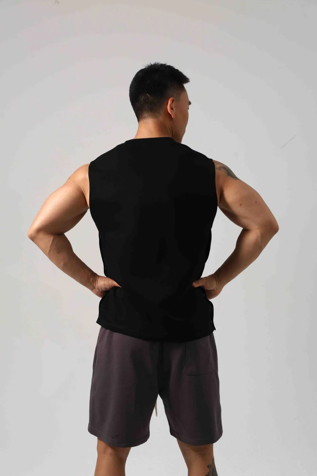 Male model wearing a solid colour loose fit cotton fitness vest with hidden side hooks.
