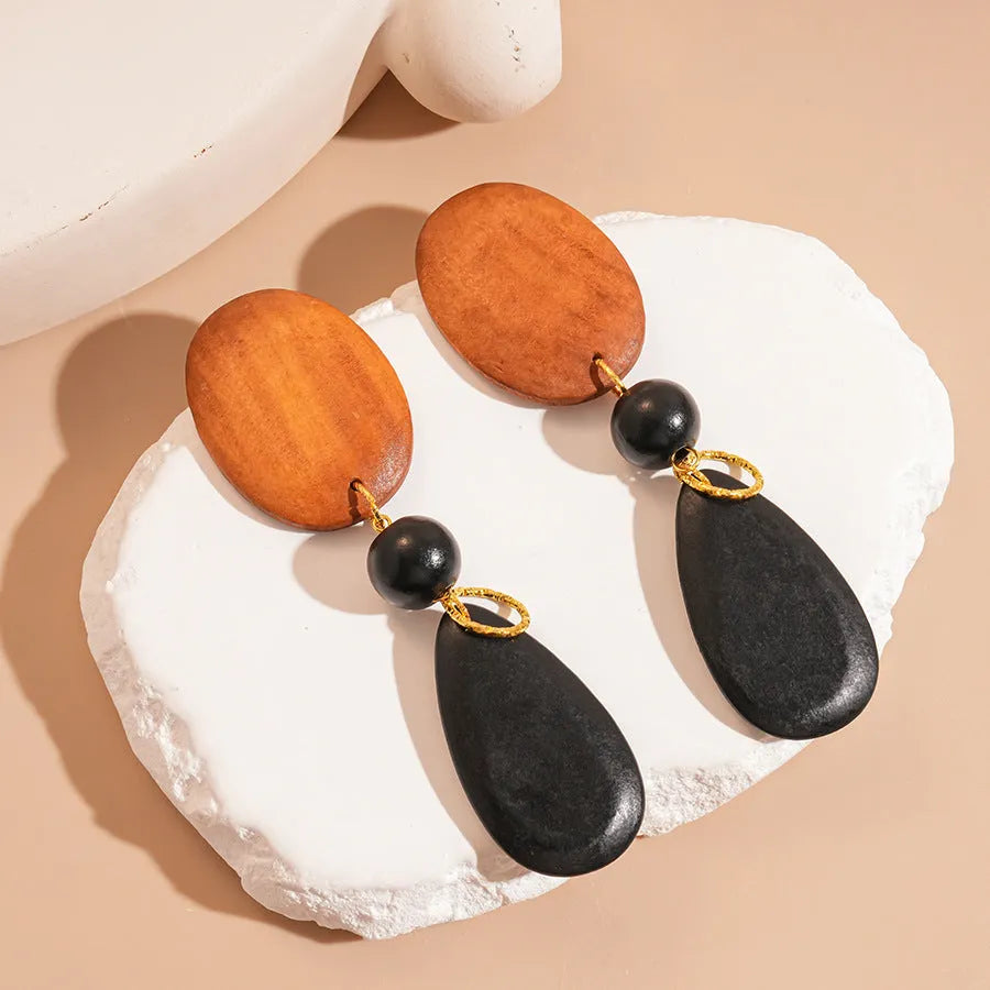 Pair of brown-black retro wooden ellipse earrings for women on a plain background.