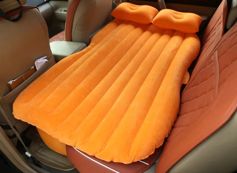 Inflatable car bed with flocking material shown in vehicle with two pillows and storage bag
