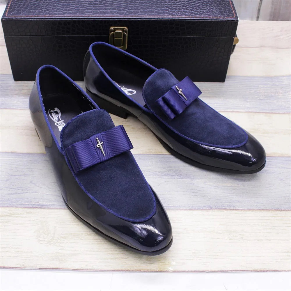 Men's glossy black patent leather tassel loafers with a low-top design and rubber sole on a wooden floor.