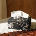 White Chinese brocade tissue box with embroidered plum blossoms on a side table.