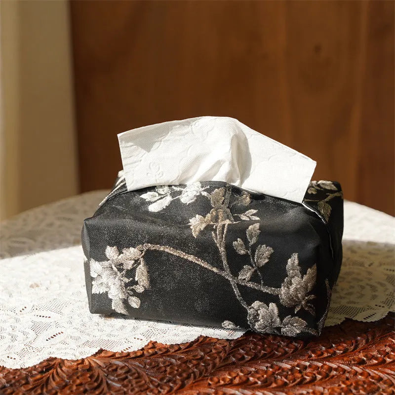 White Chinese brocade tissue box with embroidered plum blossoms on a side table.