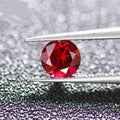 A loose, faceted cultured ruby gemstone in a pigeon blood red colour on a white background.