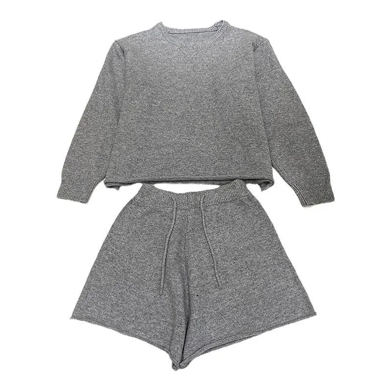 Woman wearing a loose beige knitted sweater and matching wide-leg shorts, a loungewear set on a neutral background.