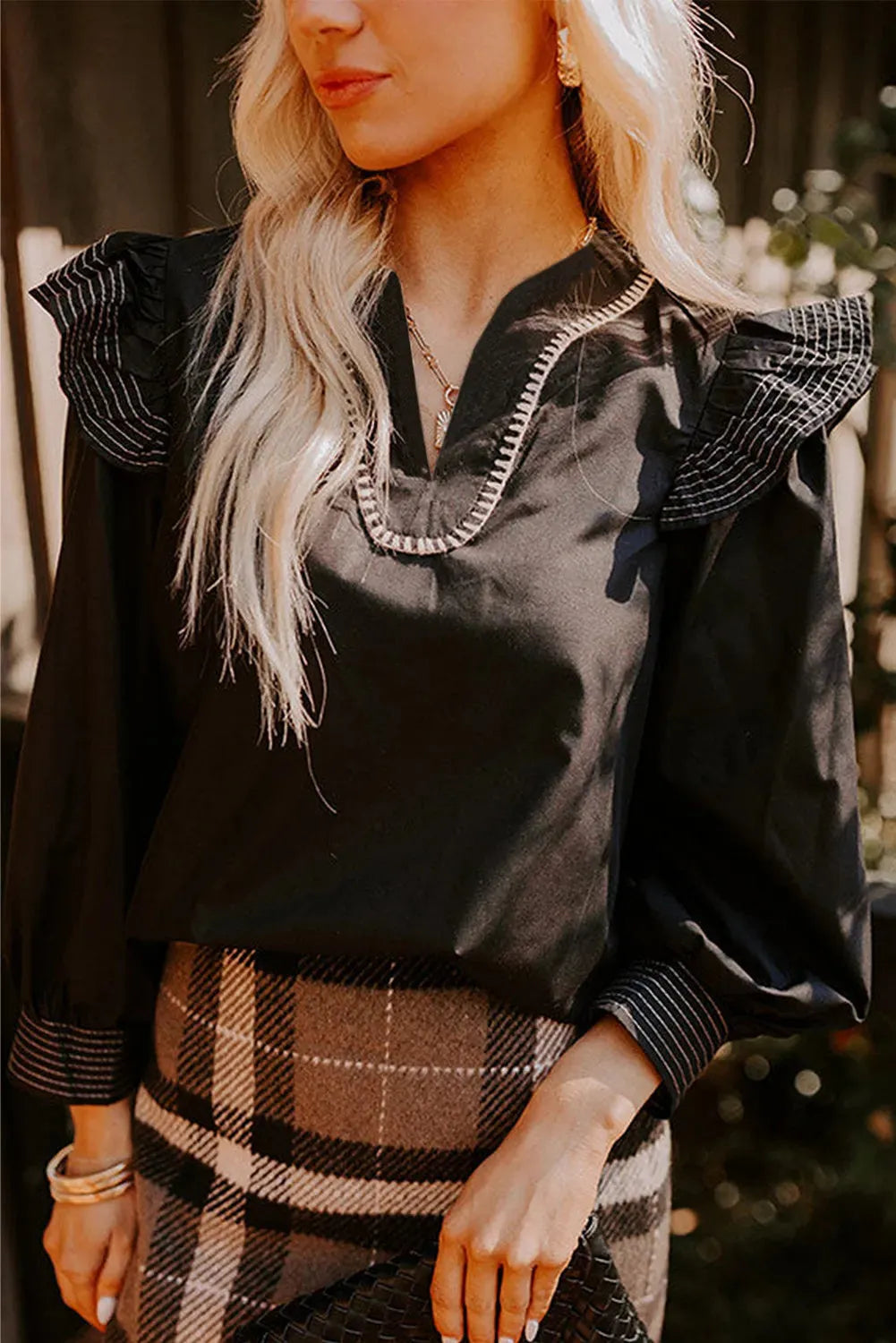 Black women's long-sleeve blouse with a V-neck, ruffle trim, and contrast stitching.