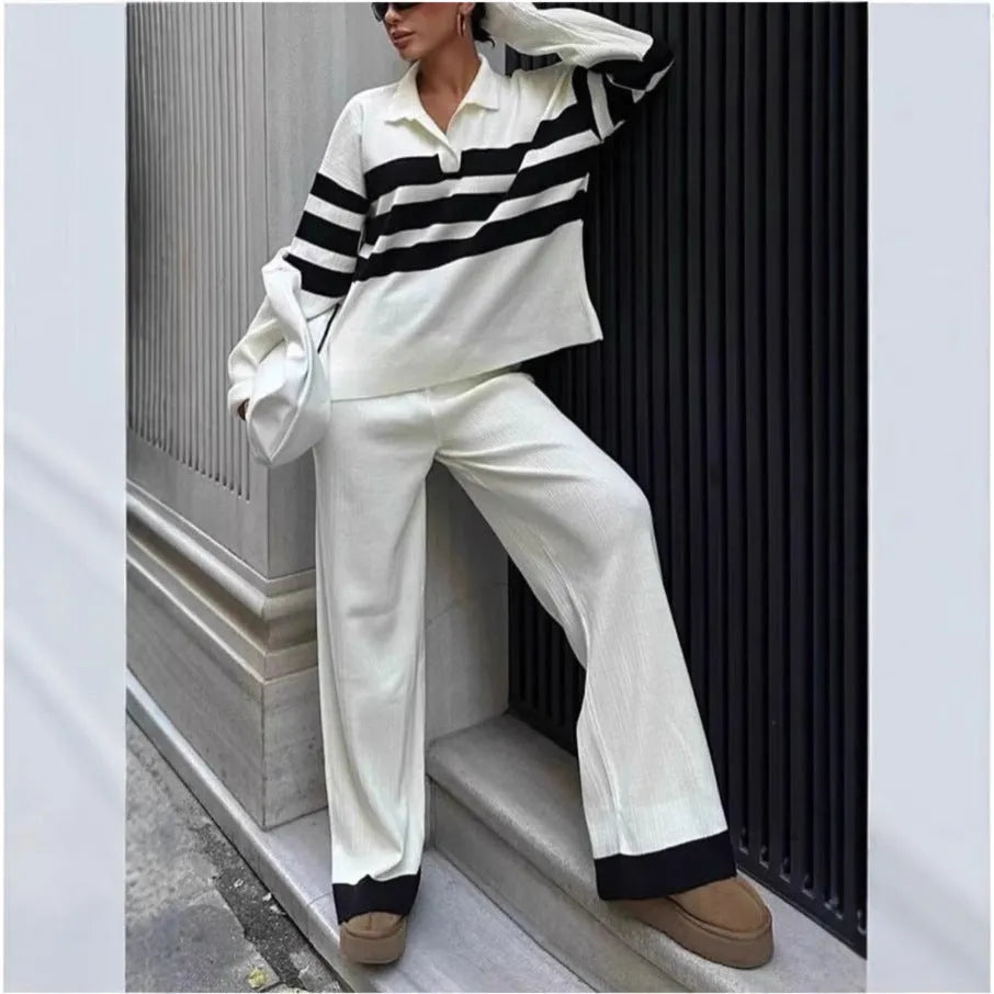 Women's black knitted polo shirt with white stripes and matching trousers laid flat.