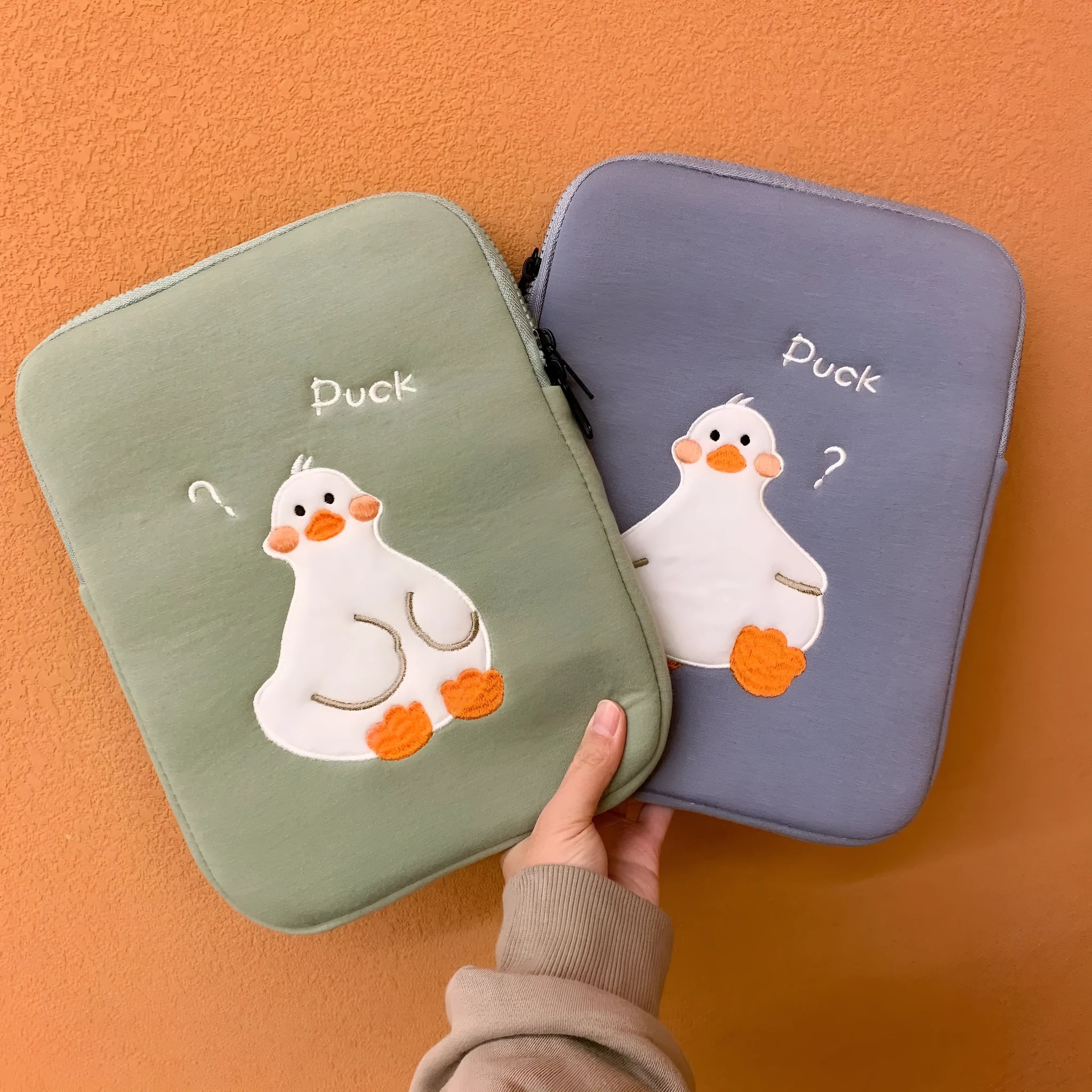 Blue cotton tablet case with an embroidered cartoon duck design and a silver zip closure.
