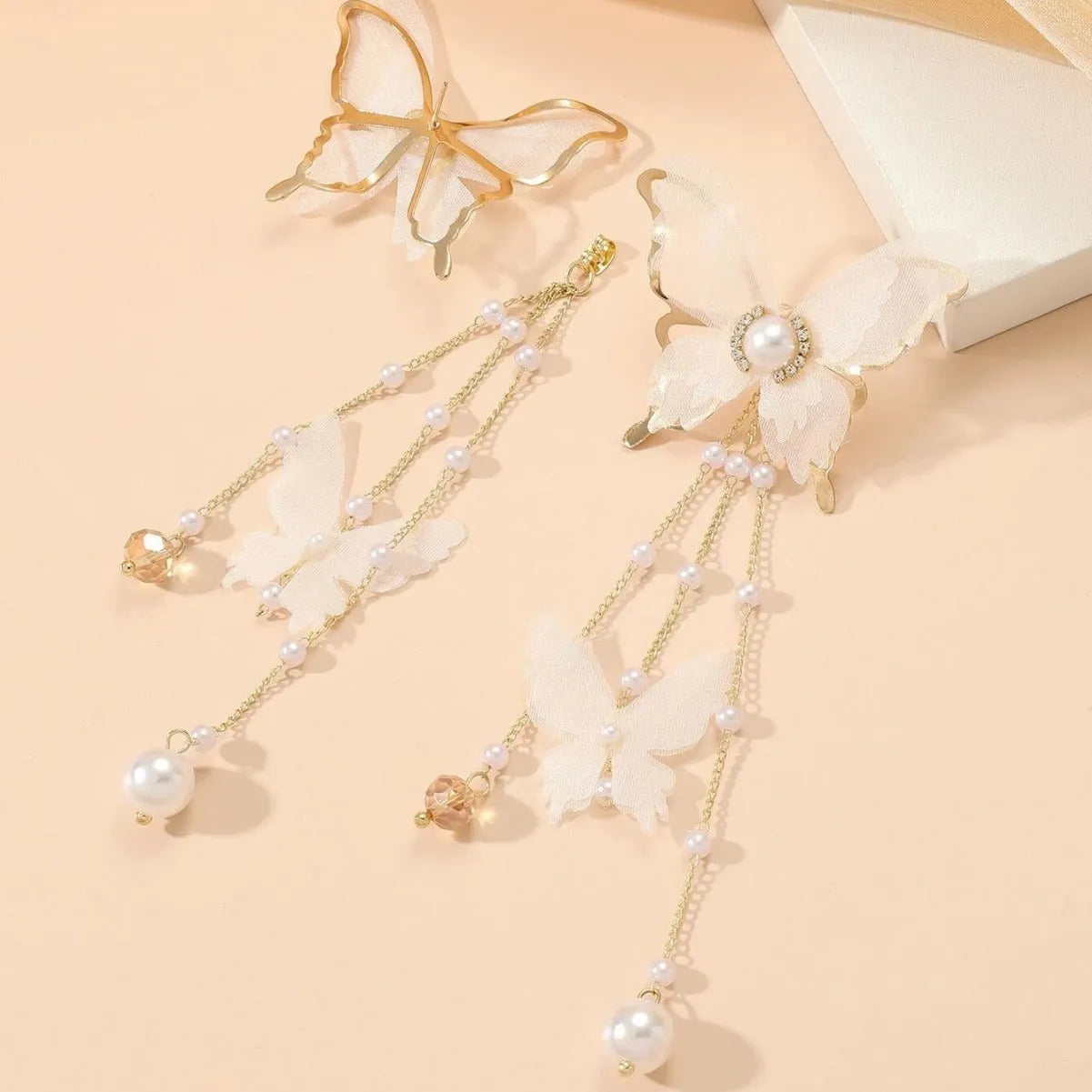 Close-up of white butterfly-shaped earrings with pearl and rhinestone details, featuring a dangling tassel on a model's ear.