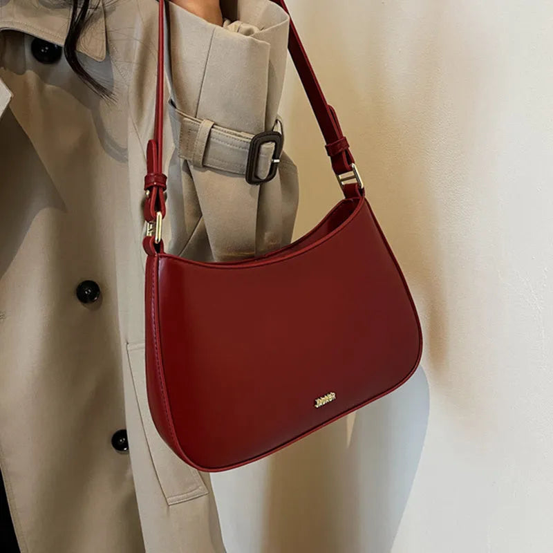 Red underarm shoulder bag in textured faux leather with adjustable strap for crossbody or sling wear