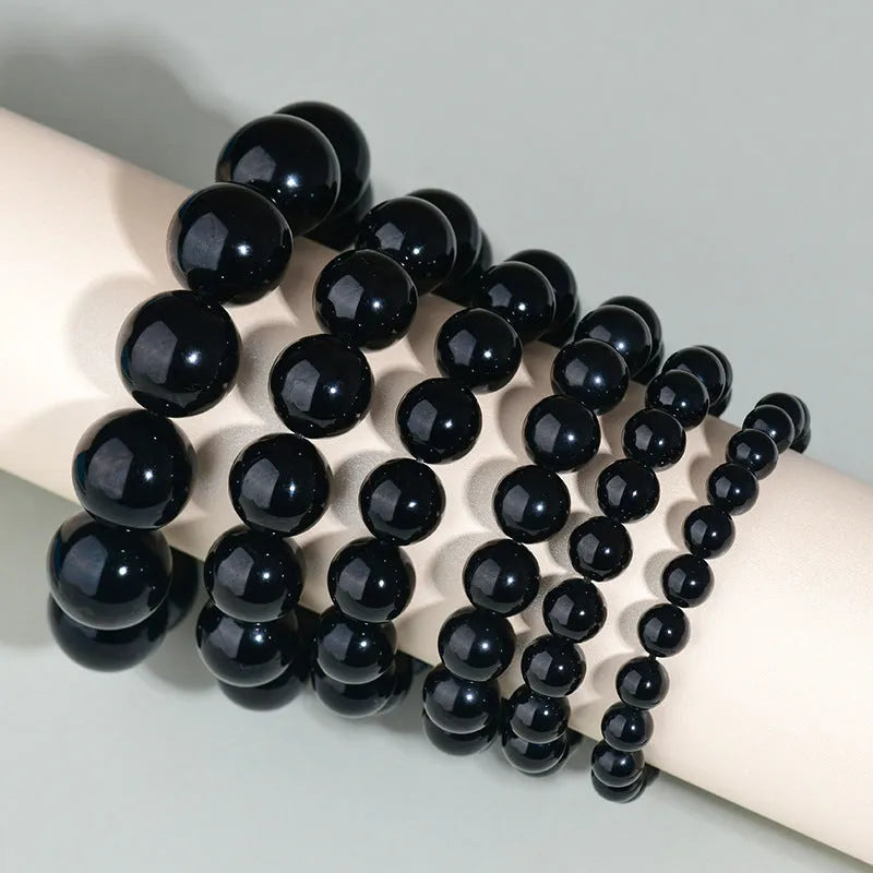 Hand-woven round obsidian crystal bracelet in black, silver, and rainbow eye colours on a neutral background.