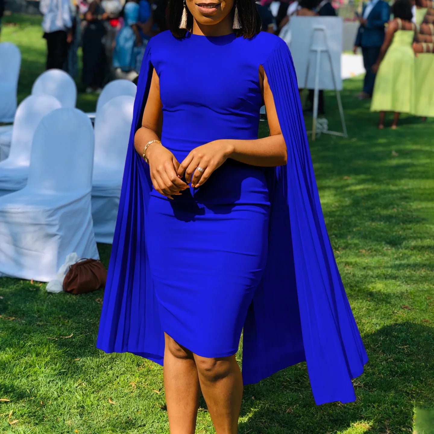 A woman wearing a long sleeve, high-waist pleated evening gown in a solid colour, showcasing the floor-length skirt and round neckline.