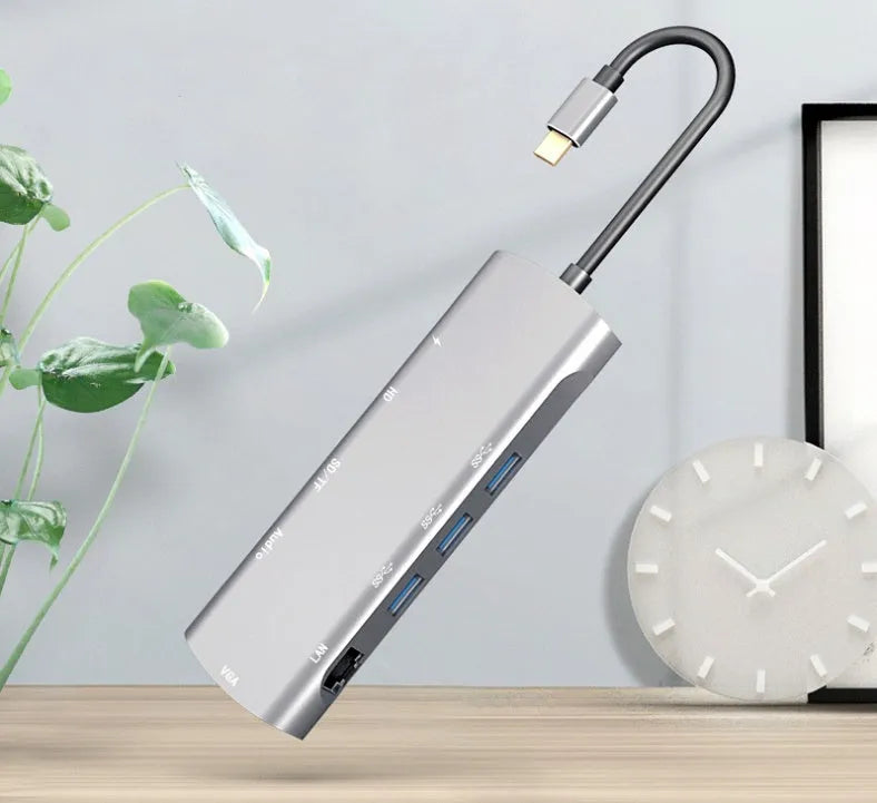 Grey aluminium USBC docking station with HDMI, VGA, USB 3.0, and charging ports on a desk.