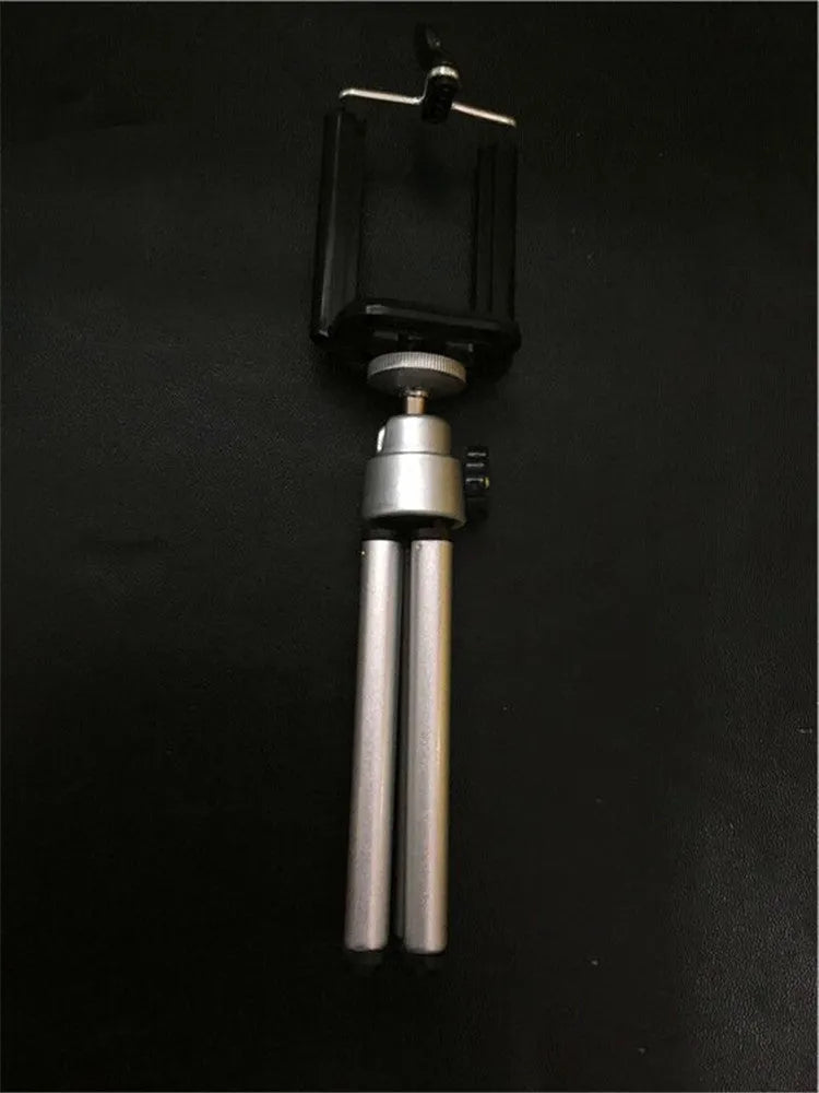 A black or silver desktop phone holder with a two-section adjustable bracket on a wooden desk.